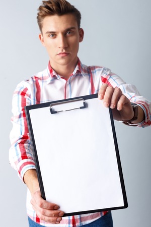 Look at this document. Portrait of cheerful young man showing a folder to camera. He is standing and looking forward with seriousness. Isolatedの写真素材