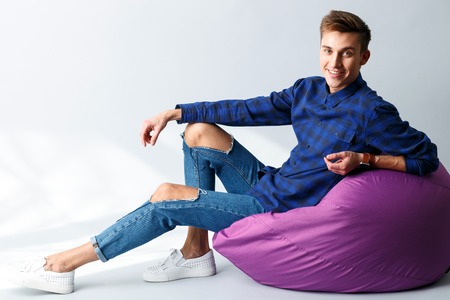 Portrait of handsome young man sitting and relaxing on flexible chair. He is looking at camera and smiling. Isolatedの写真素材
