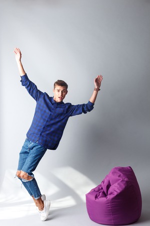 Full length portrait of handsome young man standing and falling on flexible chair. He is raising arms up and looking at camera with disappointment. Isolatedの写真素材