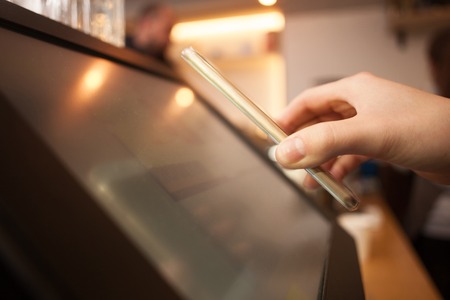 Close up of female hand holding a mobile phone near a screen. The woman is scanning on the payment machine by NFCの写真素材