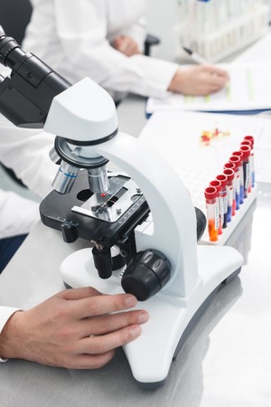 Close up of arms of scientists doing research in lab. Man is looking at samples through the...