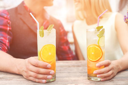 Cheerful man and woman are dating in cafeteria. They are talking and smiling. Focus on glasses of cocktail in their handsの写真素材