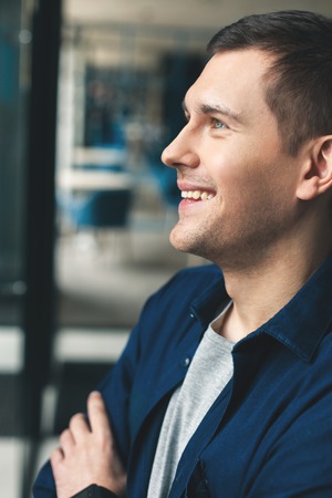 Cheerful young man is standing in profile. He is looking forward and smilingの写真素材