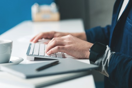 Close up of male hands typing on a keyboard. Man is sitting at desk near documentsの写真素材