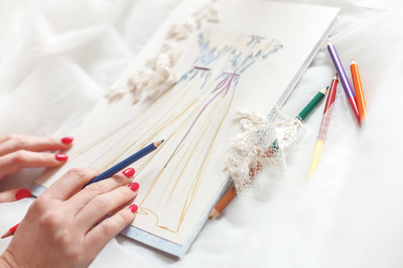 Close up of female hands drawing sketch of wedding dress. Designer is holding a pencilの写真素材