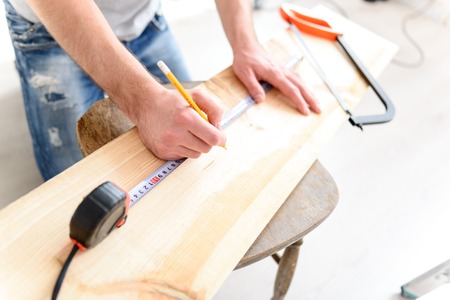Working that wood. Top view of male hands measuring piece of wood by tape measure