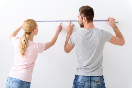 All measurements - accurate. Happy young couple measuring their new empty apartment, using measurement tapeの写真素材