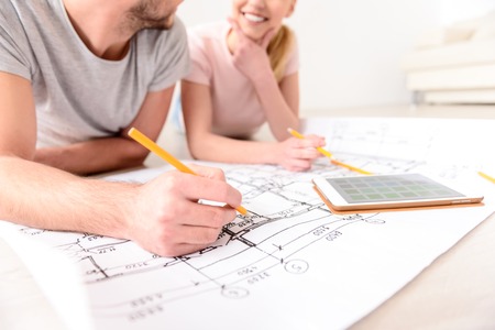 Close up of couple lying on floor of their new apartment and making marks on plan, using pencil