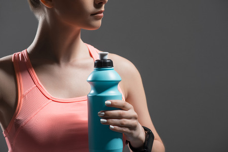 Close up of cheerful young sportswoman holding a bottle of water. She is standing in sportswear. Isolated and copy space in right sideの写真素材