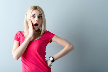 Portrait of attractive young woman opening her mouth with shock. She is standing and raising arm to face. Isolated and copy space in right sideの写真素材