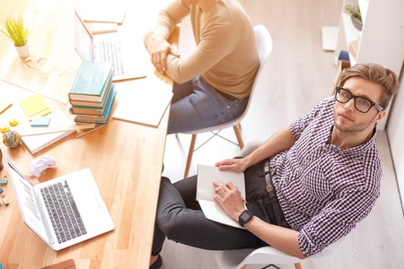 I making most of my education. Top view of guy sitting with notebook, using laptop and studing with friend in backgroundの写真素材