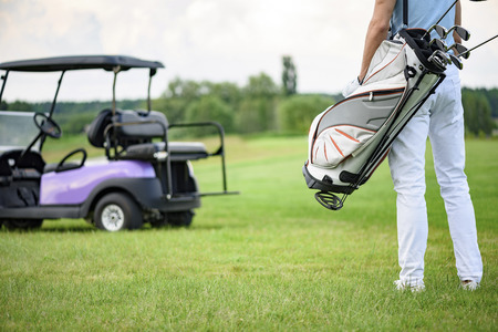 Ready to play golf. Close up of male golfer walking away holding golf back with golf cart on backgroundの写真素材