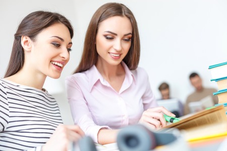Helping out a classmate. Close up of two smiling girls deciding task, studying together for upcoming exams with guy in backgroundの写真素材