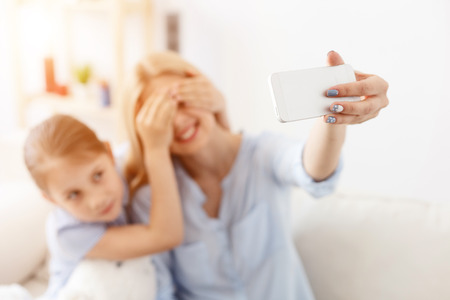 Cherishing every moment together. Smiling mother and daughter taking selfie while spending time at homeの写真素材