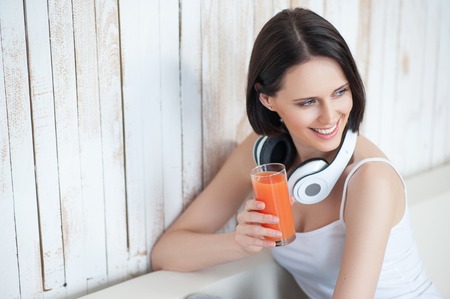 Enjoying refreshing start to day. Top view of young woman enjoying drink of orange juice with headphones, sitting on sofaの写真素材
