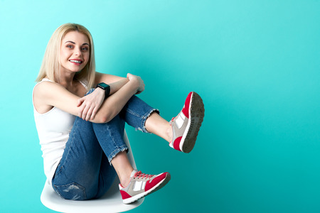 Portrait of cheerful young woman sitting on stool. She is raising her legs up and smiling. Isolated and copy space in right sideの写真素材