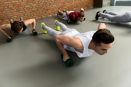 Skillful male athletes doing push-ups with efforts. They are holding weights