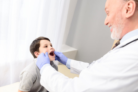 Top view of smiling mature pediatrician examining little boy throat in his officeの写真素材