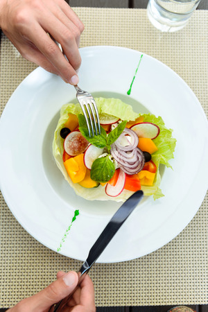 Close up of male hands holding fork and knife near a plate of salad.の写真素材