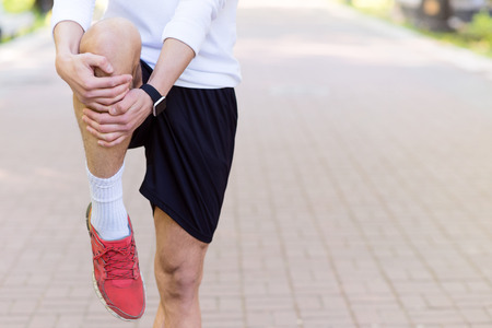 Close up of male runner warming up his leg. Man standing outdoorsの写真素材