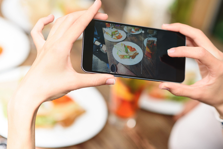 Very appetizing. Close up of woman hands taking photo food by mobile phone in cafeの写真素材
