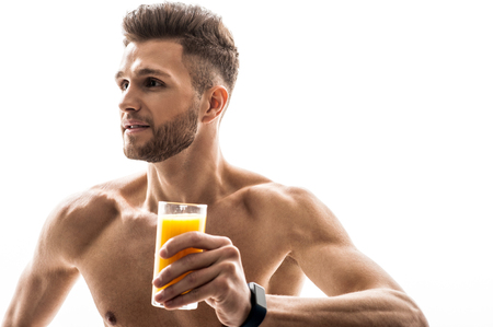 Juice is good for my healthy. Joyful fit man is holding a glass and smiling. He is standing and looking sideways with happiness. Isolatedの写真素材