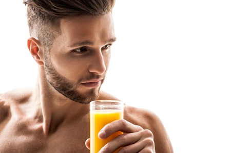 Pensive young man is holding glass of juice. He is standing and looking aside seriously. Isolated and copy space in right sideの写真素材