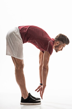 Cheerful male athlete is exercising with concentration. He is bending his body while stretching arms...