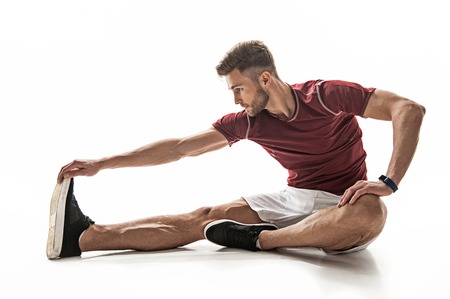Fit young man is doing exercise with concentration. He is stretching hand to foot while sitting on...