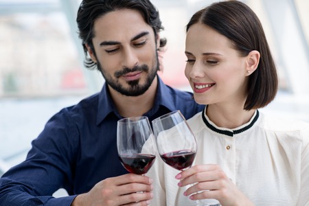 Happy loving couple is celebrating anniversary. They are clinking glasses of wine and smilingの写真素材