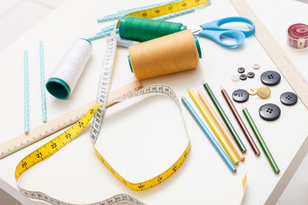 Close up of tape-line, thread, pencils, button and scissors of table in atelier
