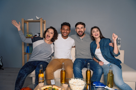 Let good times flow. Happy football fans celebrating victory of their team with beer and popcorn at homeの写真素材
