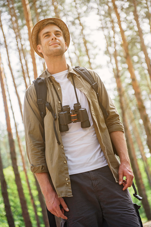 Relaxed young tourist is walking in forest with enjoyment. He is looking forward and smilingの写真素材