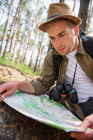 Skillful male tourist is reading a map of location in forest seriouslyの写真素材