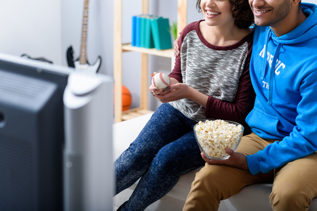Our game is on. Cropped photo of young couple sitting on couch at home and watching tennis game with popcornの写真素材