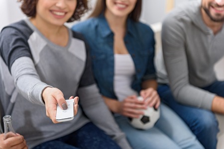 What on this channel. Cropped photo of smiling girl holding TV remote with friends in backgroundの写真素材