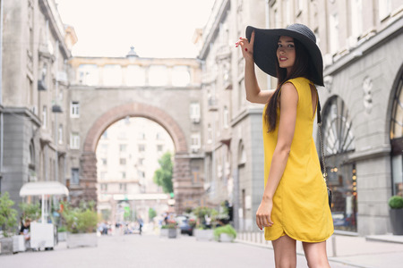 Joyful young girl is having walk in city. She is looking back flirtingly. Lady is touching her...