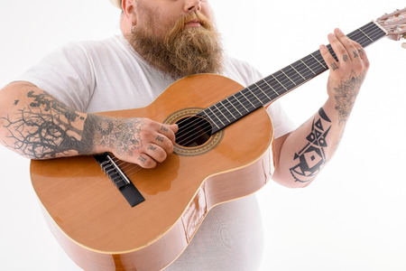Close up of thick guitarist preforming music with inspiration. Focus on guitar