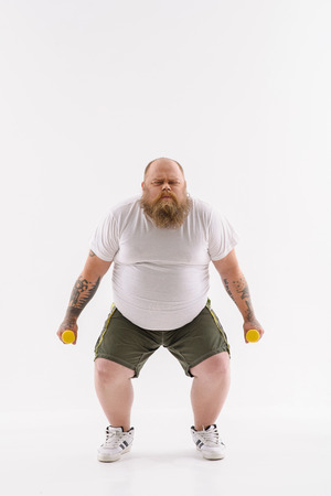 Strained fat man is trying to lift weights. He is standing and posing with efforts. Isolatedの写真素材