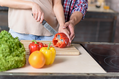 Close up of young woman cutting vegetable in kitchen. Man is touching female hand with gentlenessの写真素材