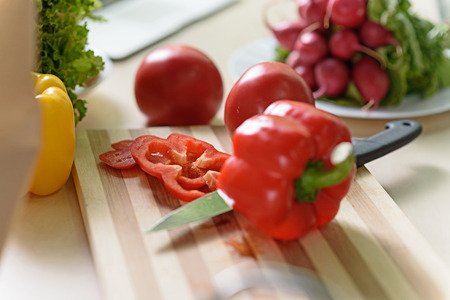 Close up of chopped pepper on board near knife. Tomato and radish on background