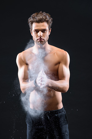 Sexy young man is applying white chalk on hands before training. He is standing and looking at camera with confidence. Isolatedの写真素材