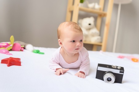So much to see. Cute little baby girl lying on bed next to toys and looking away with wonderの写真素材