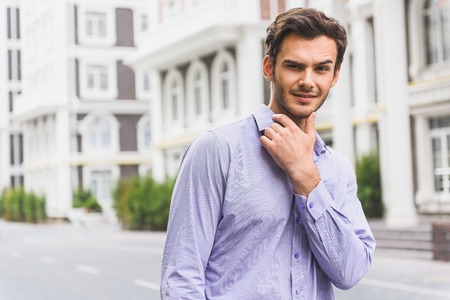 Attractive young businessman is looking forward with interest and flirting. He is standing on street and smilingの写真素材