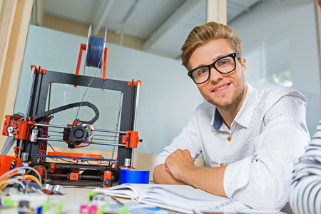 Happy male engineer using 3d printer in office. He is looking at camera and smiling