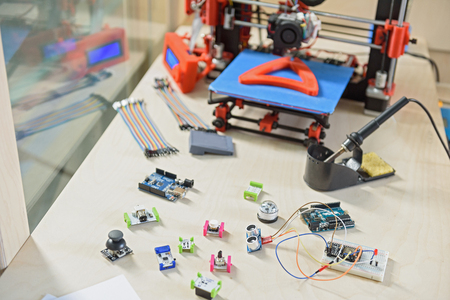 Modern 3d printer with its details on table in office
