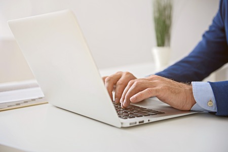 Close up of hands of man in suit working on digital tablet and sitting at desk in officeの写真素材