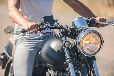 My bike is the best. Close up photo of guy sitting on motorcycle and holding handlebar, turning...
