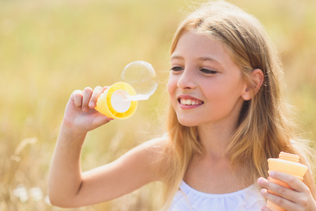 Joyful girl is blowing soap bubbles with enjoyment. She is standing on field and laughingの写真素材