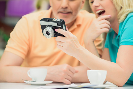Senior married couple is watching photos on camera. They are sitting at table in cafeteria and smilingの写真素材